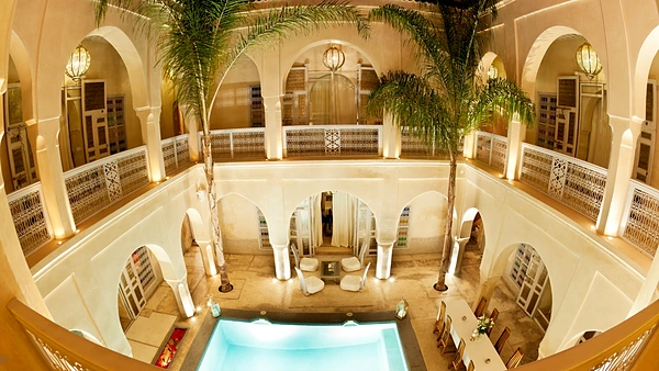 Patio d’un riad de luxe vu d’en haut : arcades, palmiers, lanternes et piscine éclairée
