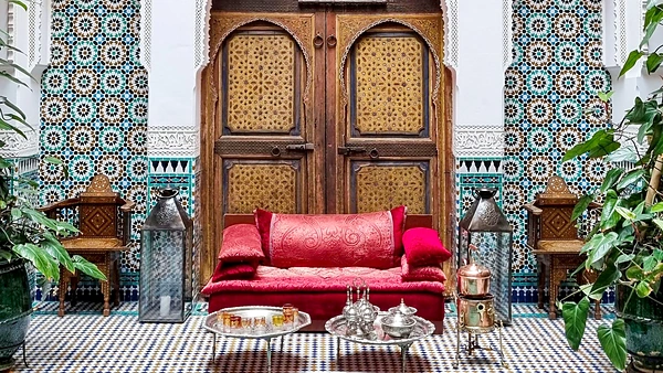 Salon d’un riad traditionnel : banquette de velours rouge, porte en cèdre sculpté, murs de zellige et service à thé en argent