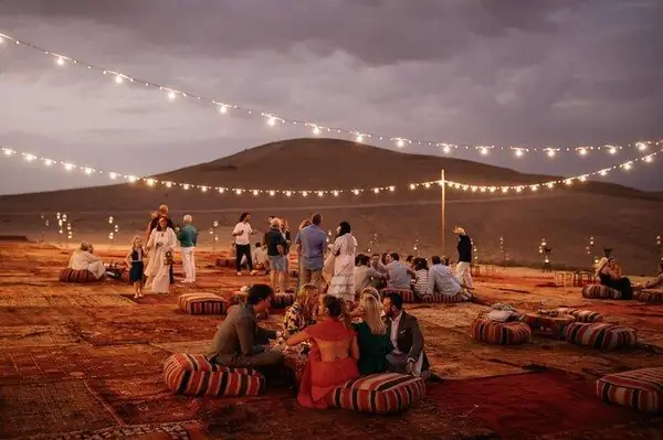 Group seated on rugs and cushions under string lights, Agafay desert