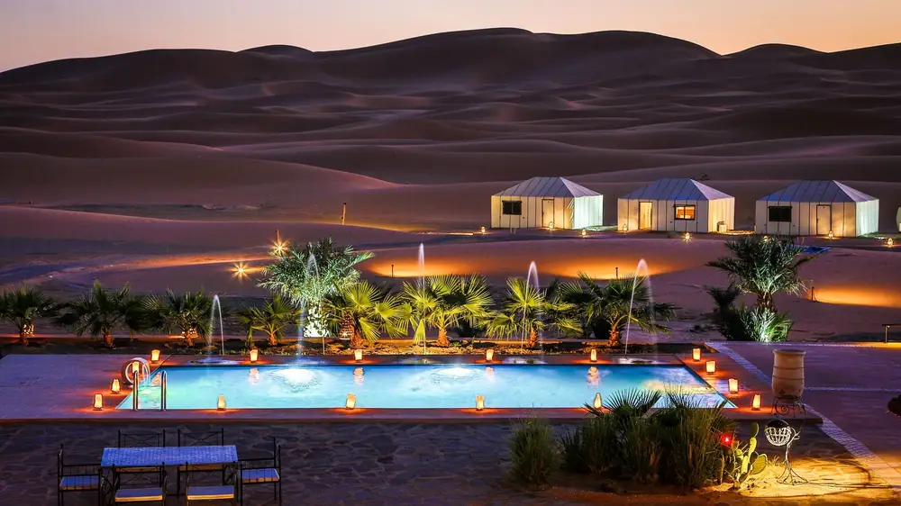 Luxury camp and its pool lit up at the foot of the dunes